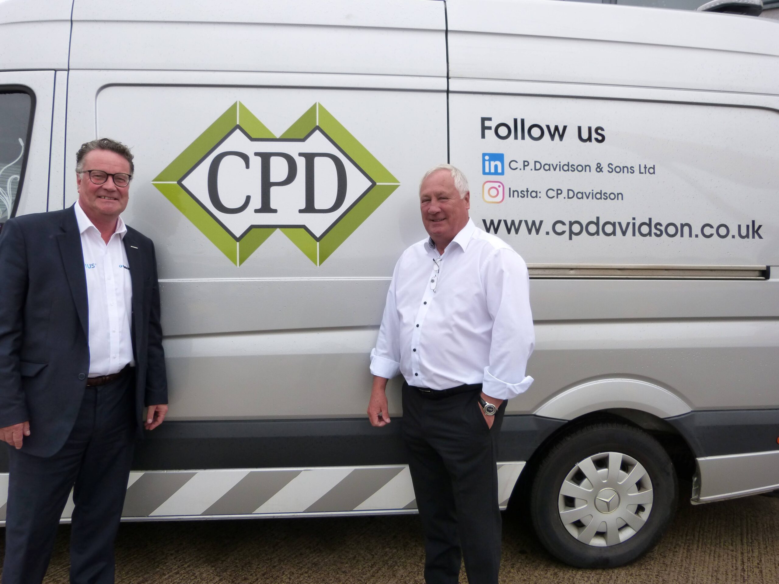 Standing in front of a white transit van, with the C.P Davidson logo and either side of the logo, is Simon standing to the left, wearing a white shirt and navy suit. And the other side standing is Philip wearing a white shirt and black trousers.